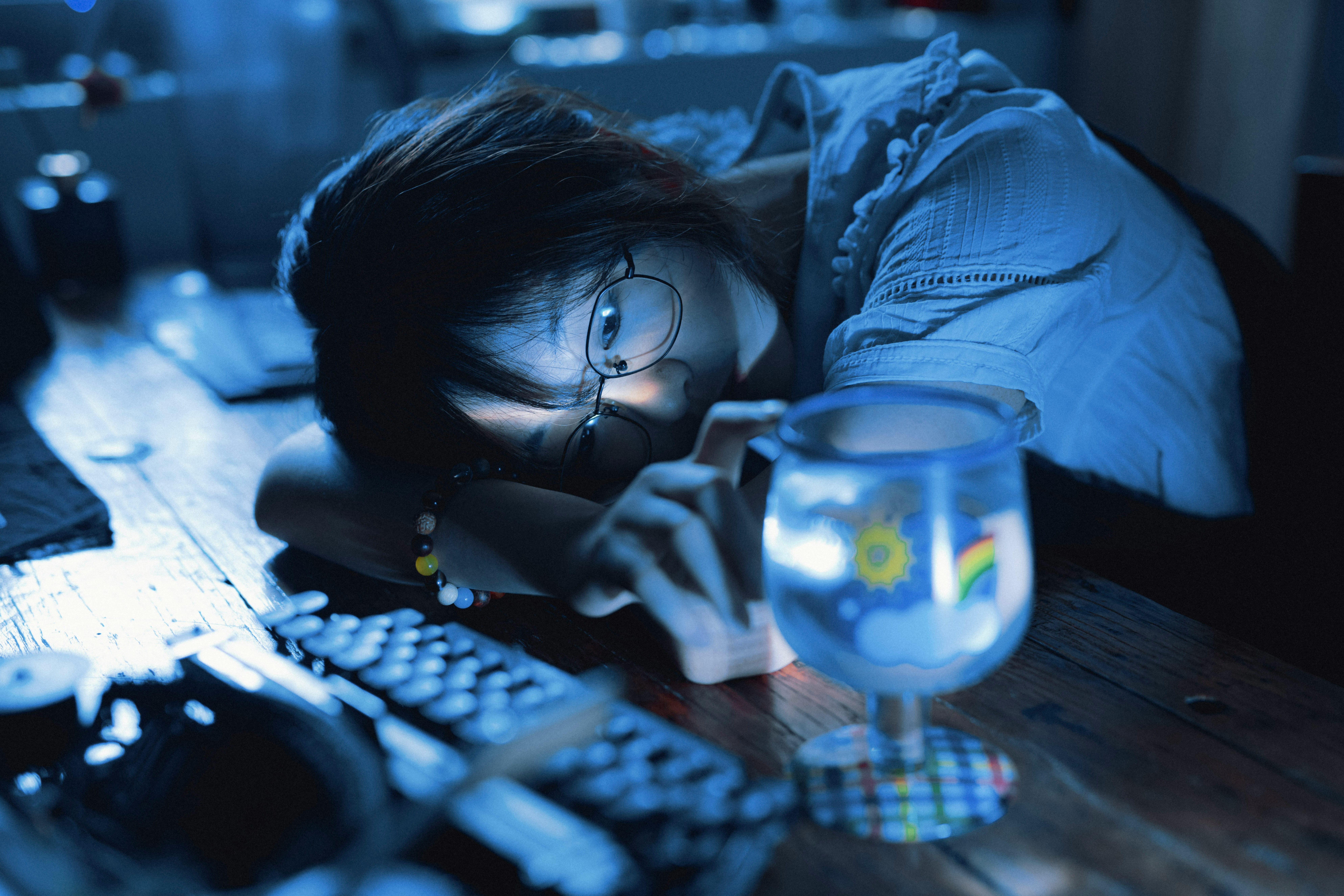 Woman lit by phone screen, resting her head on the table, lost in thought.
