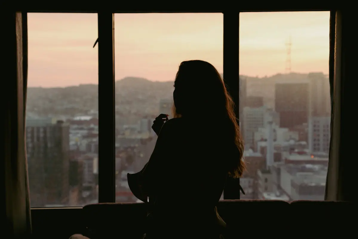 Woman sitting alone by window reflecting after being ghosted